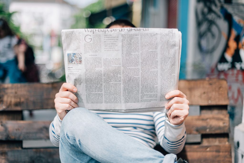 Personne lisant un journal en se couvrant le visage.
