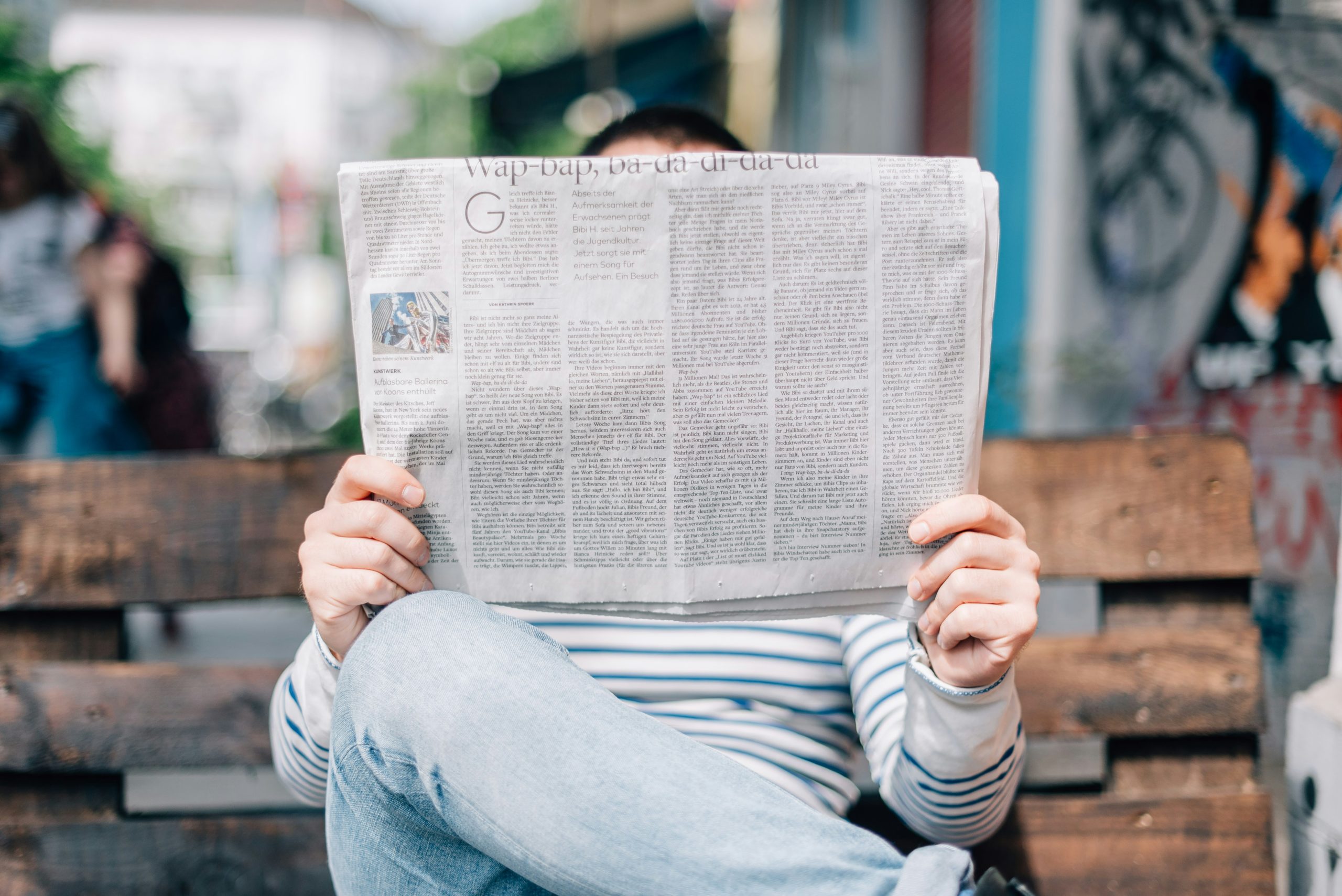 Person reading a newspaper covering their face.